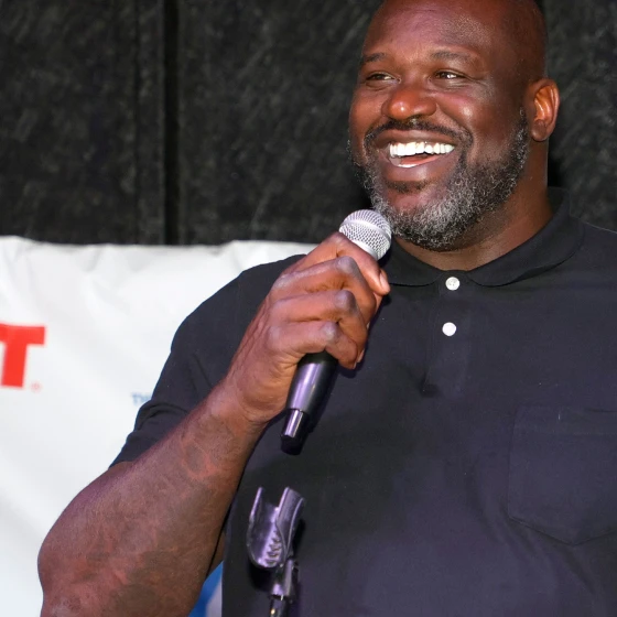 Shaquille O'Neil speaking at the inauguration of one of the Las Vegas Comebaq Court. He's holding a microphone on his right hand as he smiles. The Icy Hot logo can be seen in the background.